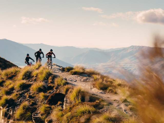 Three mountain bikers on top of mountain with mountain range in background