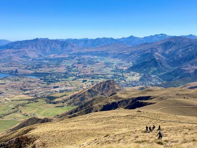 Group of bikers riding down Crown Peak overlooking view of mountains and town
