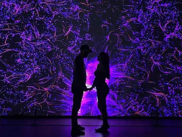 Couple holding hands in front of illuminated art installation