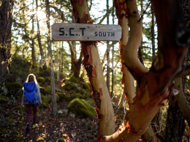 A woman hikes past a sign on the trail that says "S.C.T. South."