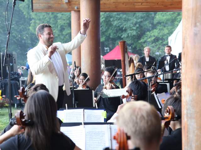 A man stands in front of music students conducting a performance.