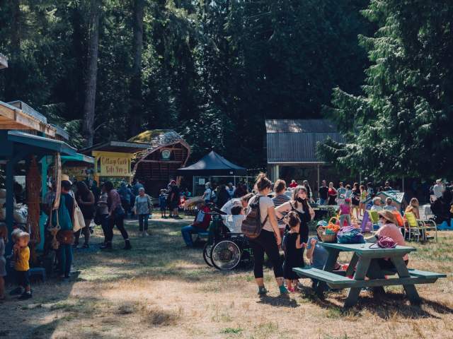 A view of people browsing market stalls and gathering around nearby picnic tables.