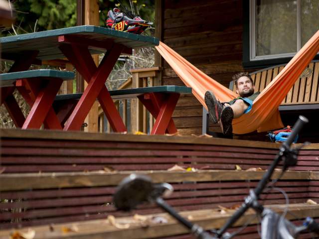 A man relaxes in a hammock with at the lodge with his bike and helmet resting nearby.