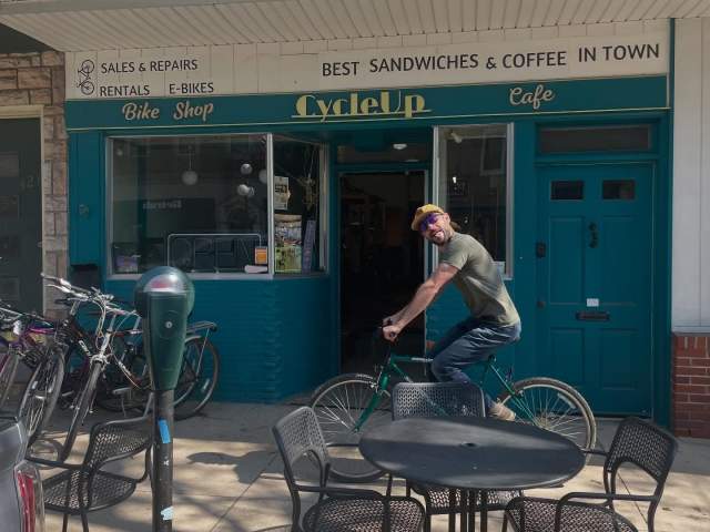 Picture of CycleUp Cafe + Bike Shop owner Chris riding a bike in front of the shop.