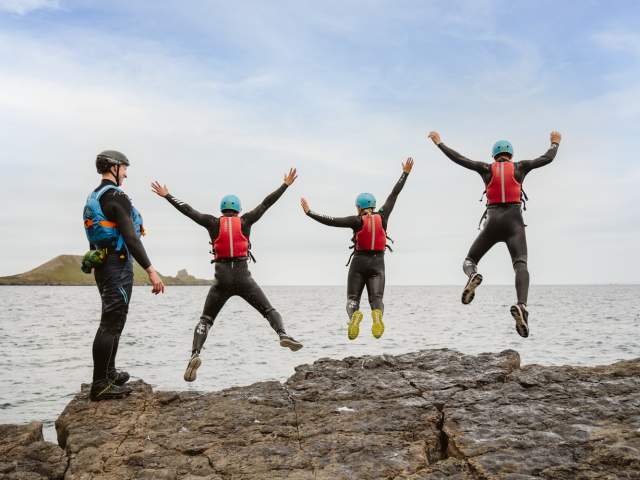 Group of people coasteering and jumping into water while instructor watches on
