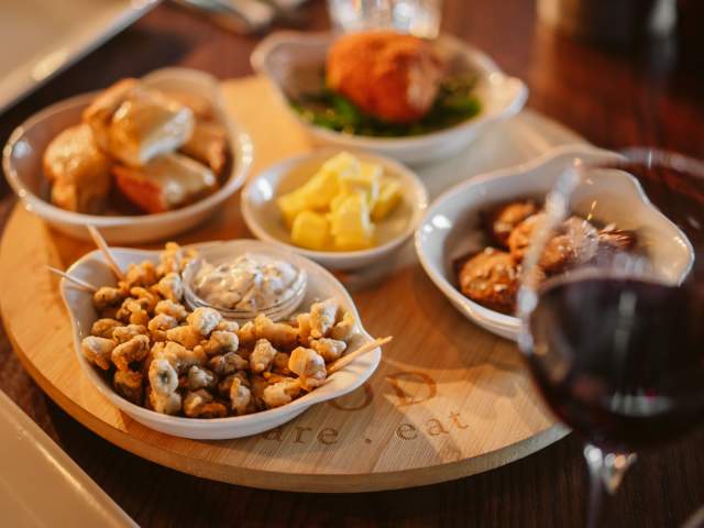 Battered cockles in a bowl with a glass of red wine.