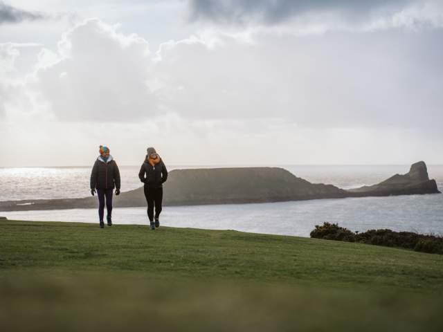 two young women walking along the coast with worms head in the background