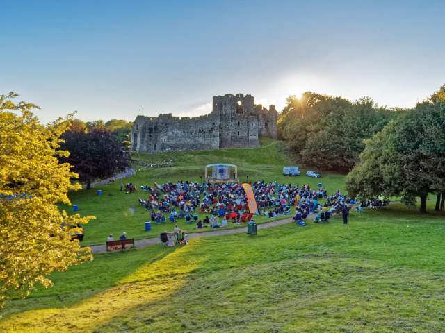 theatre performance with crowd watching on with oystermouth castle in the background at sunset
