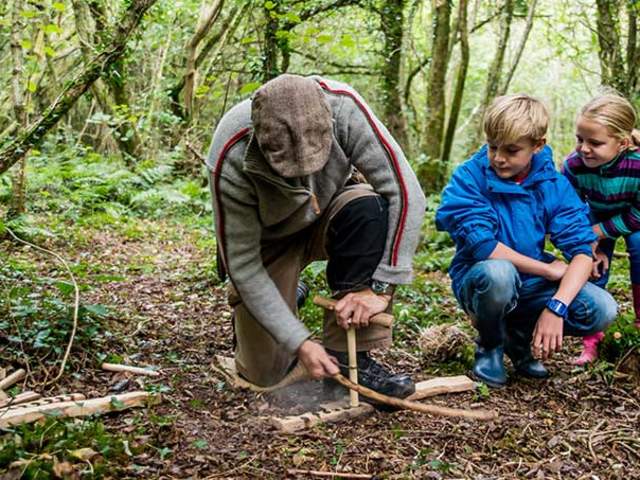 A man teaching two children how to start a fire using sticks
