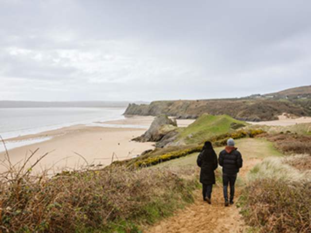 A couple walking on a sandy path by Three Cliffs Bay