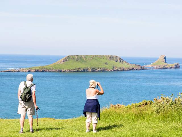 An older couple at Rhossili looking out to Worm's Head. The woman is using binoculars.