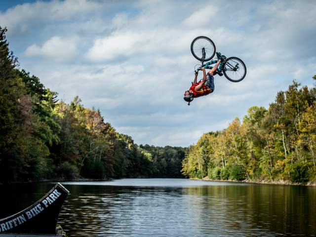 Stunt biker going off a ramp and flipping upside down over water at Griffin Bike Park, Terre Haute, Indiana