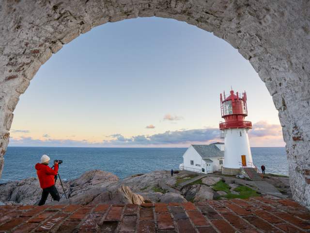 Kvinne i orange jakke fotograferer Lindesnes Fyr