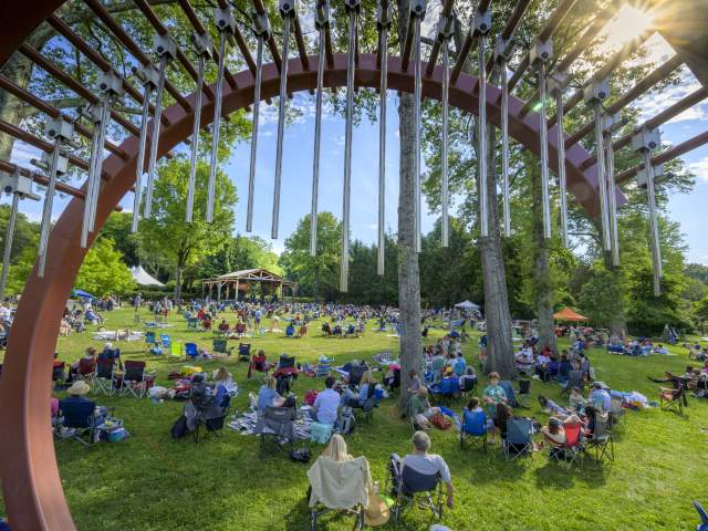 A photo of a crowd on the lawn taken from behind a piece of artwork shaped like a "C".