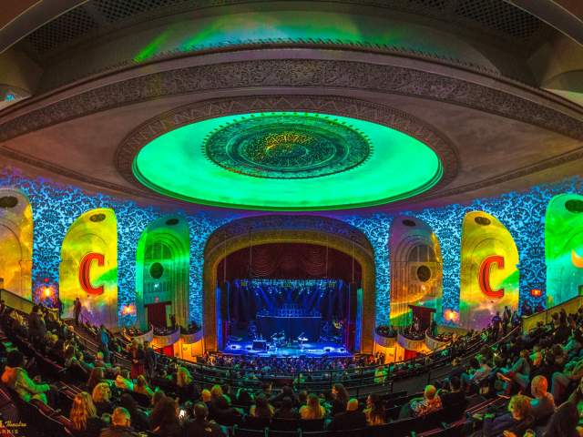 A crowd is gathered for a concert inside The Capitol Theatre. The room is awash in green and yellow lighting.