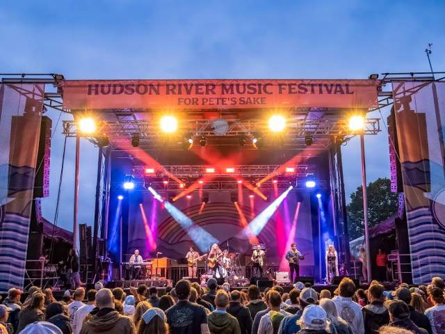 The stage at Hudson River Music Festival with multiple blue and red lights and a crowd.