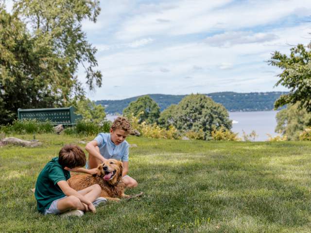 Two children pet a dog while sitting on the lawn of Lyndhurst, overlooking the Hudson River.