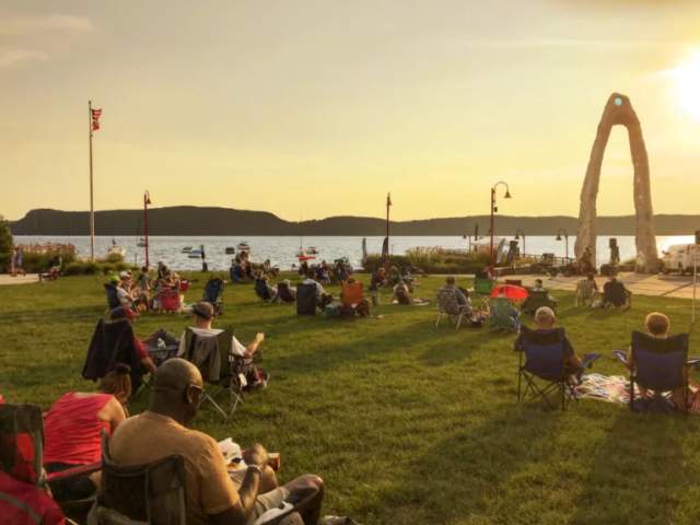 A group of people in lawn chairs sit at a park bordering the Hudson River.