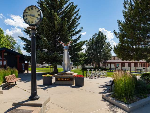 a standing clock tower and jackalope statue in a quaint park in Wyoming