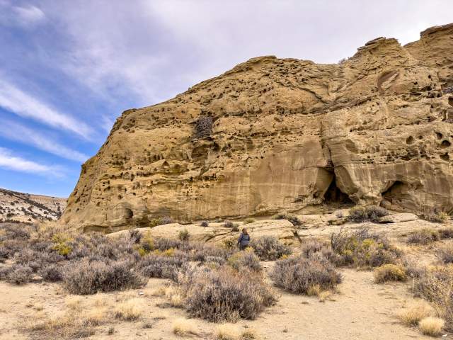Rugged geologic formations rise high above low bushes in Rock Springs under a cloudy blue sky.