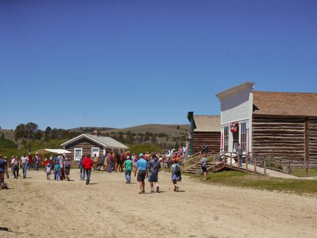 A group of tourists walks toward historic houses at South Pass City, with mountains rising in the distance.