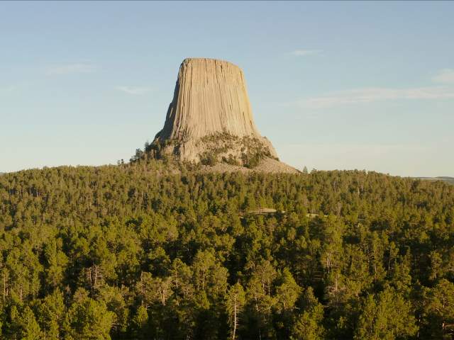 Aerial view of Devils tower above treeline and a blue sky