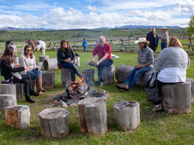 Patrons enjoying wine and a campfire at a ranch.