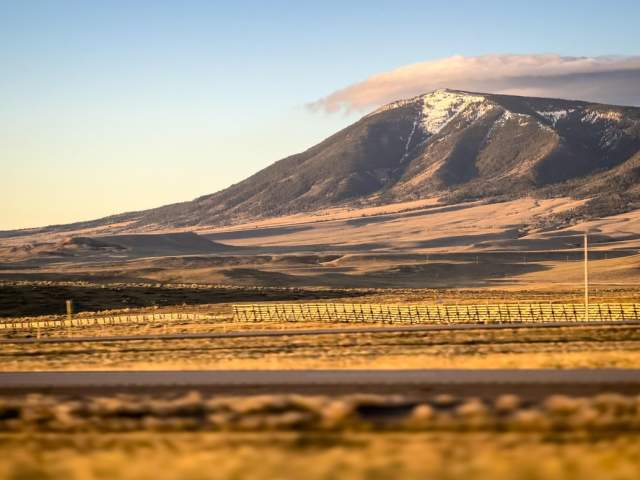 A sprawling golden landscape with snow-dusted Elk Mountain, its peak touching gray clouds.