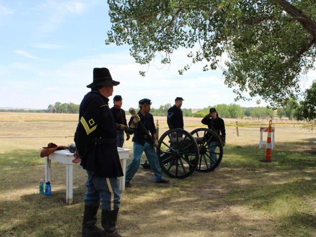 A group dressed in historic attire stands near wagon wheels at Fort Laramie National Historic Site.