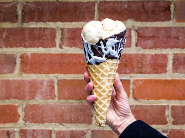 vanilla ice cream with a chocolate-dipped cone in front of a brick wall