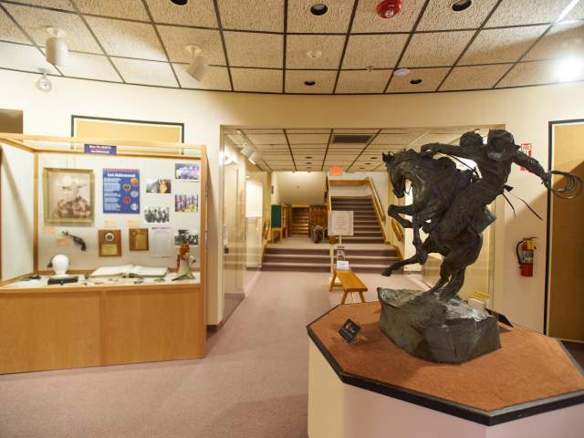 A museum exhibit features glass-encased memorabilia and a sculpture of a cowboy on horseback mid-air.