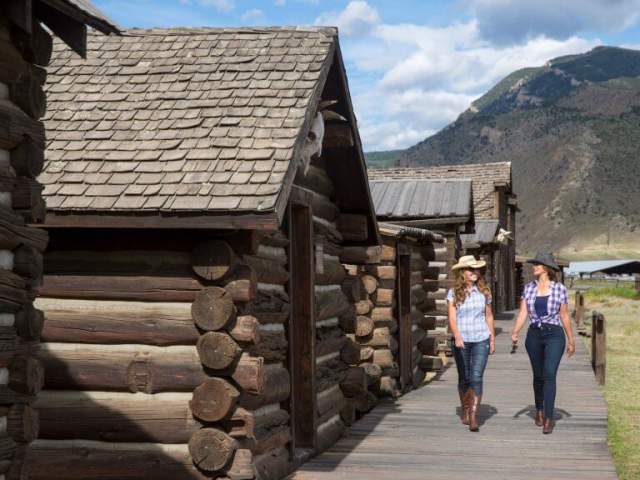 Two women walk alongside Old Trail Town, one of the top things to do in Cody WY, wearing cowboy hats and boots.