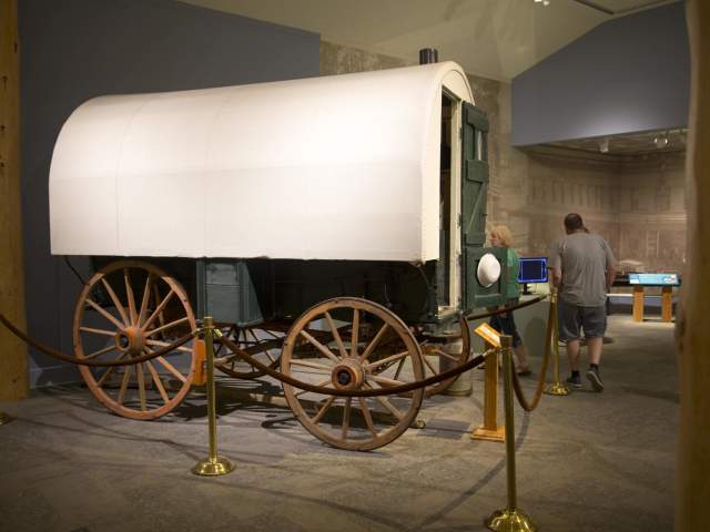 People viewing an exhibit of a covered wagon inside the Buffalo Bill Center of the West.