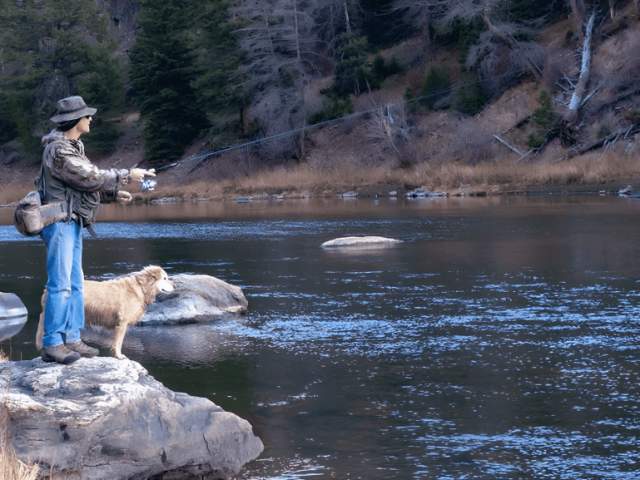 A person enjoying fly fishing in Saratoga, Wyoming with their loyal dog by their side, one of the many exciting things to do in the area.