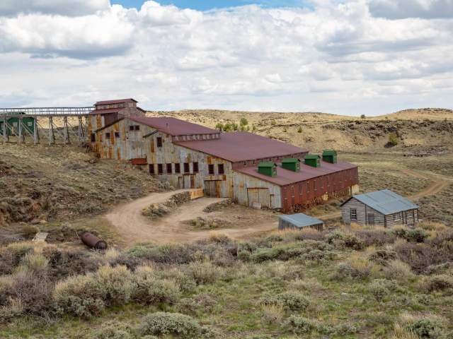 Historic structures from Carissa Mine at South Pass City, surrounded by a landscape of desert brush and hills.