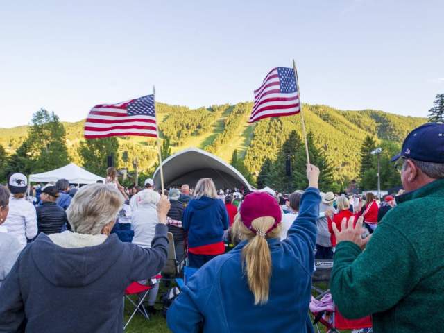 A crowd gathers, waving American flags, at an outdoor event.