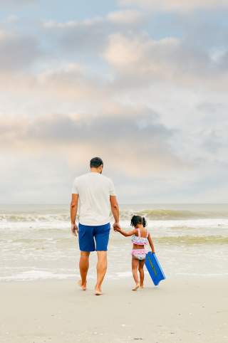 a father and daughter walk along the beach