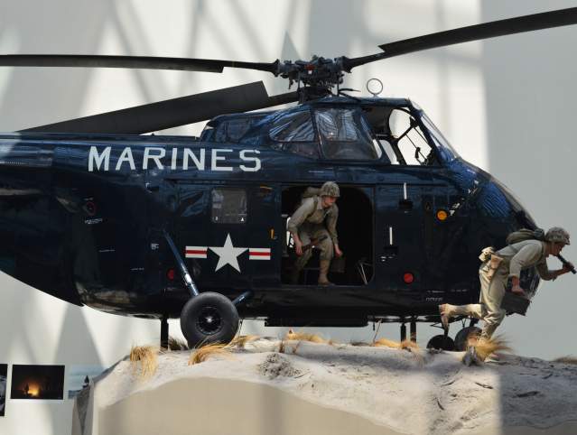 a navy helicopter with the word "marines" on the front with 2 statues of men coming out of the helicopter