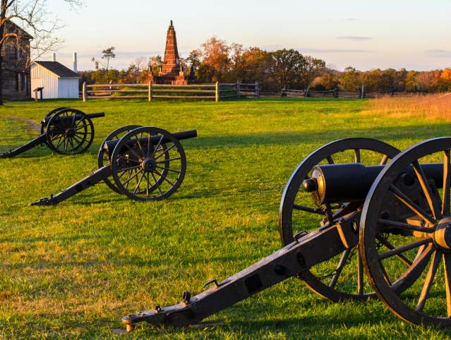 Three cannons on a battlefield with a historic house in the background