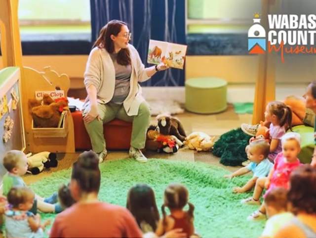 Adult reading a book to children gathered around.