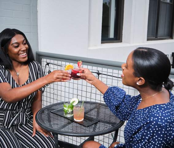 Two Black women toasting drinks at table on Abby Singer's Bistro restaurant balcony in downtown Shreveport