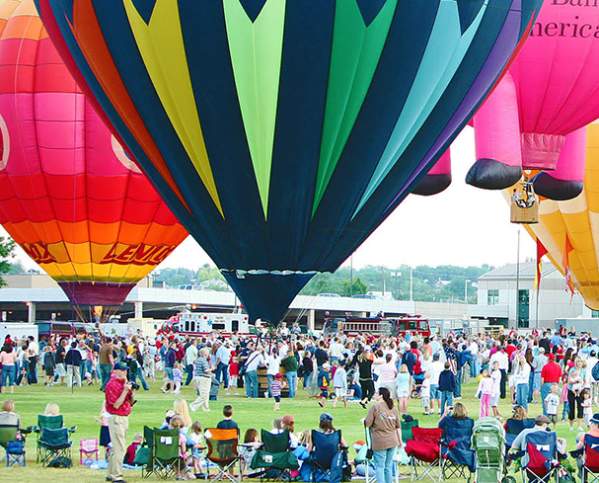 people sit in camp folding chairs and watch rising hot air balloons