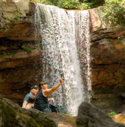 A family takes a selfie in front of a waterfall.