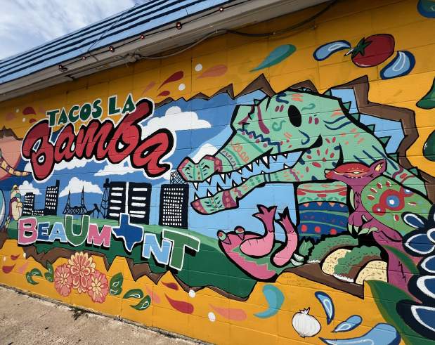 a colorful mural depicting the Beaumont skyline, alligators, flowers, tacos, and colorful patterns