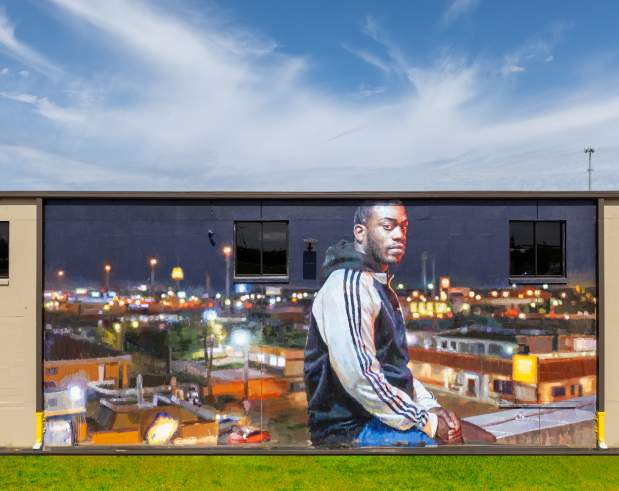 a mural showing a young man standing on a city roof overlooking the city at night