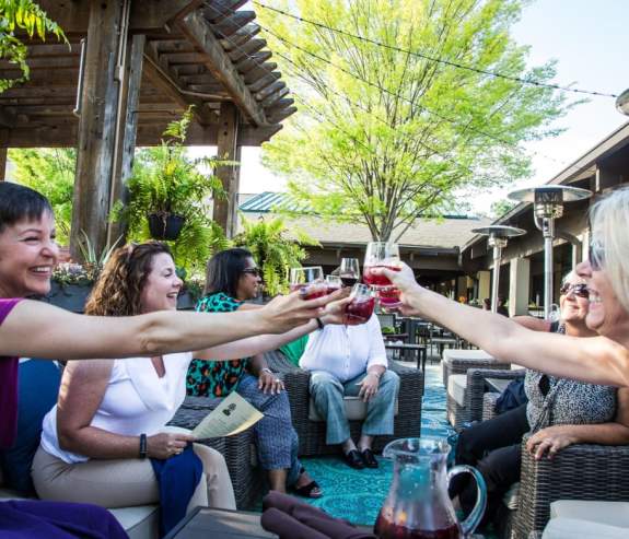 Women clinking together their wine glasses on a patio.