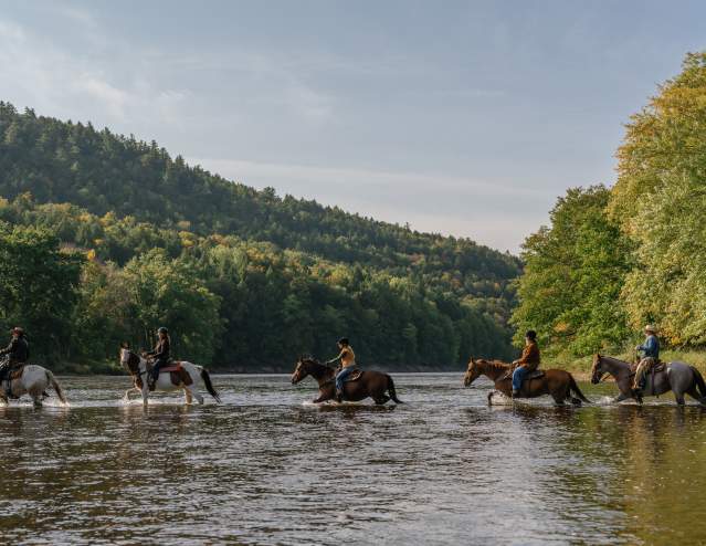 Women horseback riding across the Hudson River at 1000 Acres Ranch