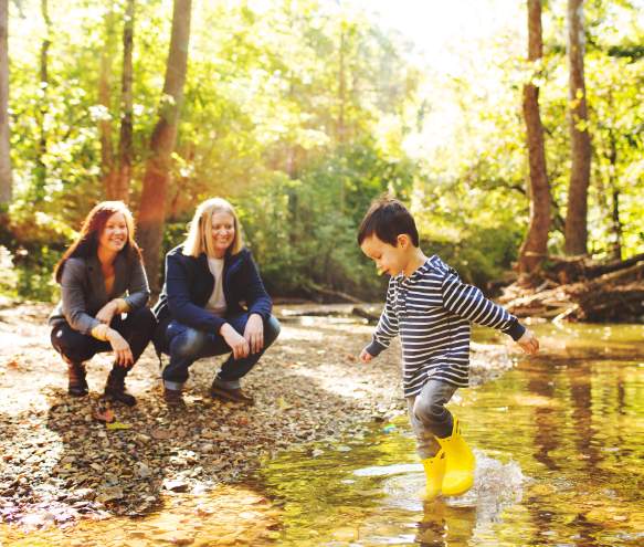 A lesbian couple watching their son play in a creek