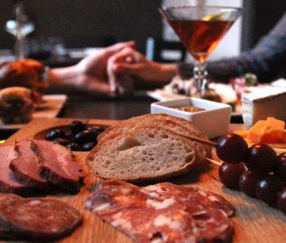 A couple holding hands at a table with a charcuterie board and martini