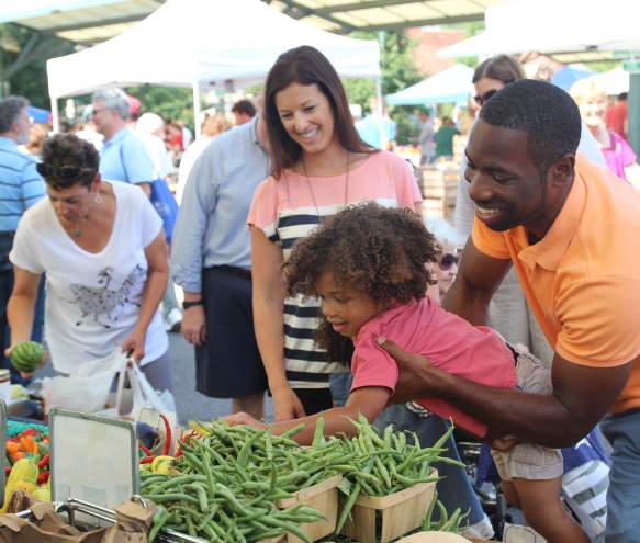 Man holding a little girl up while she selects fresh produce from the Bloomington Community Farmers Market